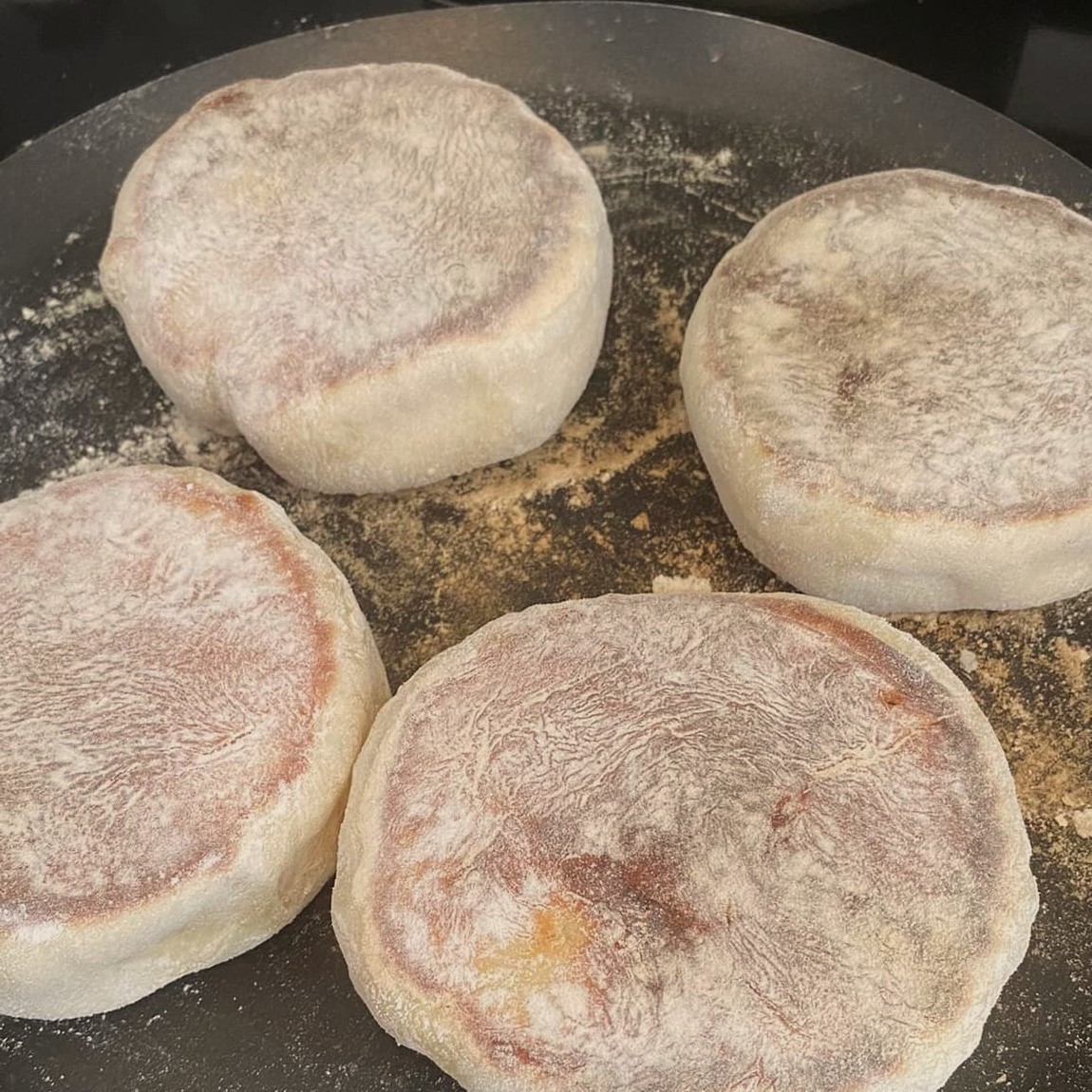 Vier Bolos Lêvedos beim Backen auf einer mit Mehl bestäubten Metallplatte