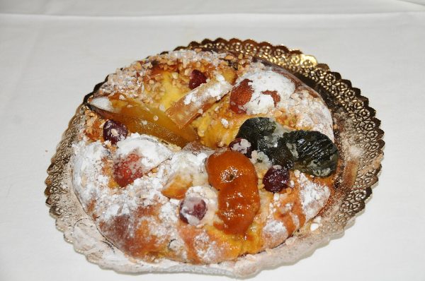 Kronenförmiger Bolo-rei mit kandierten Früchten, gehackten Nüssen und Puderzucker auf goldener Tortenspitze