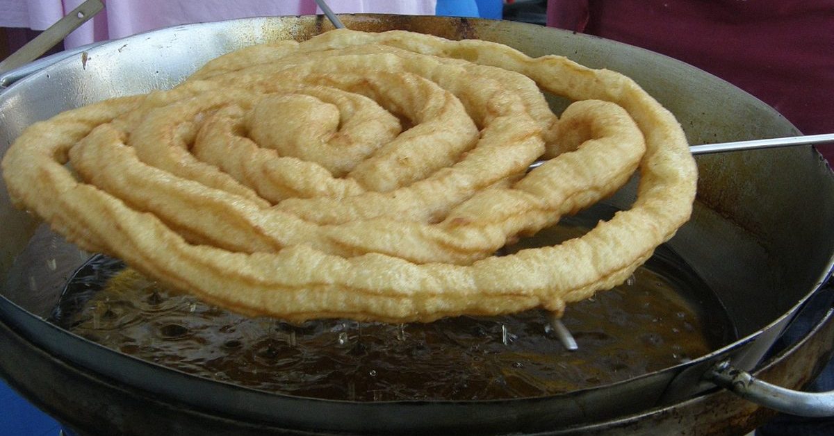 Goudbruine fartura die uit de friteuse komt op de kermis