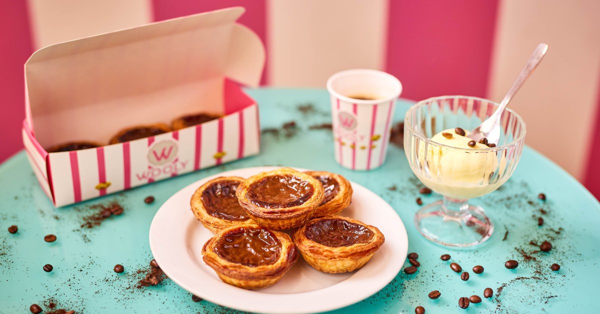 De geschiedenis van de pastel de nata: een Portugese traditie Wooly pastéis de nata op een bord, naast een koffie