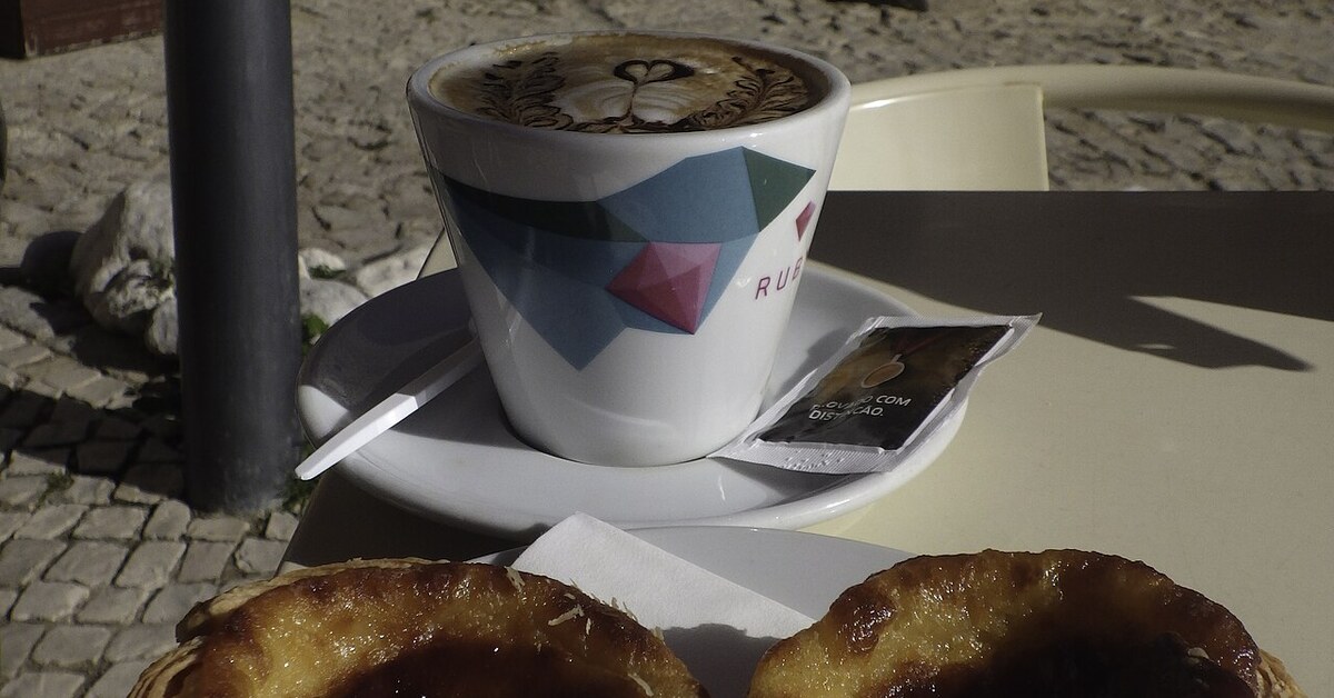Une tasse de café posée à côté d'une pâtisserie portugaise sur une table de café