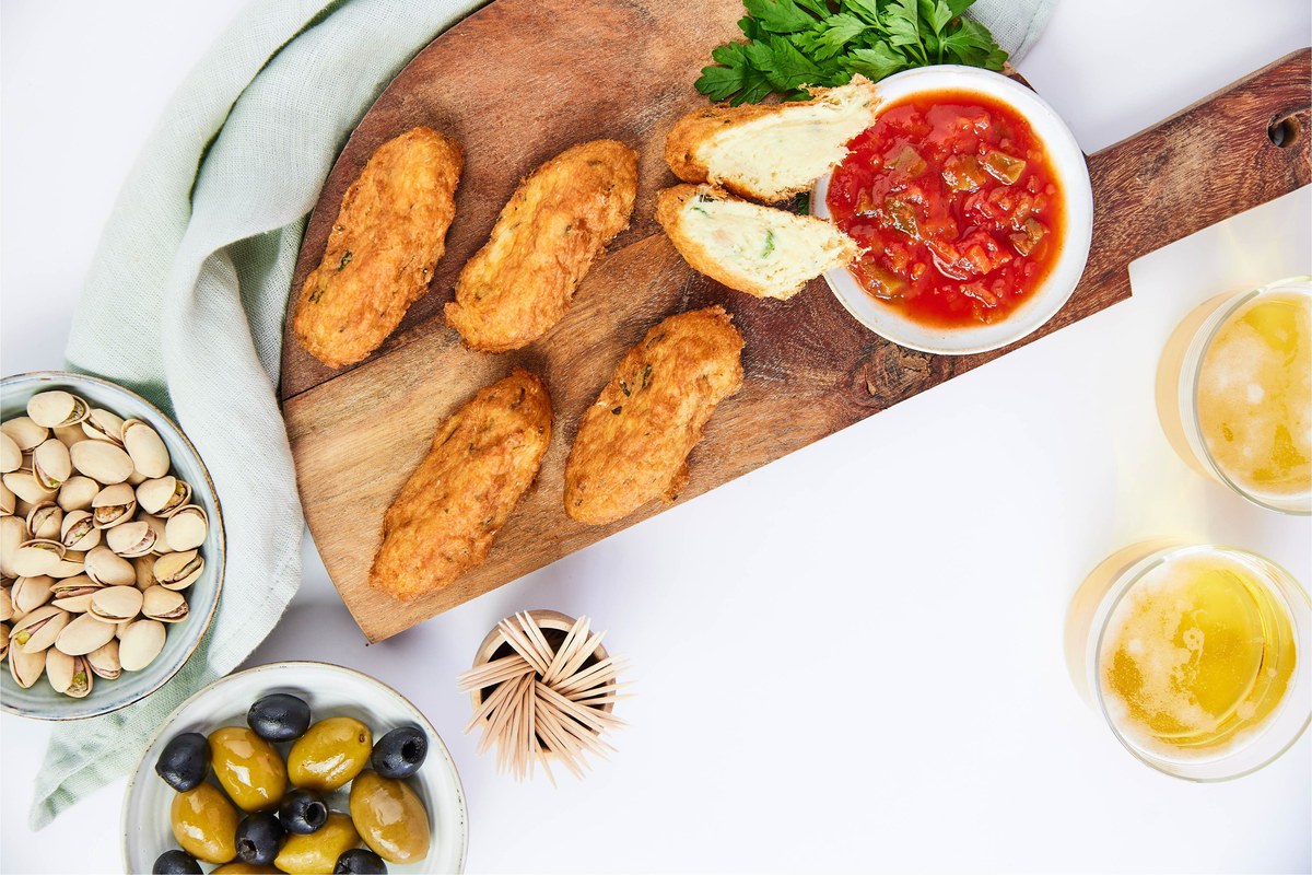 Golden pastéis de bacalhau on a wooden board, one cut in half, with tomato sauce and parsley