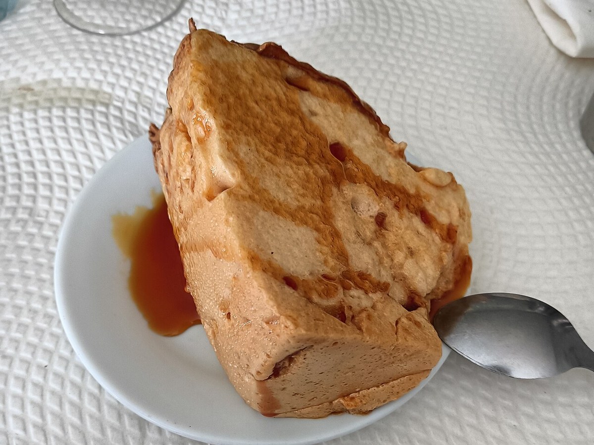 Fatia de pudim Molotof coberta de caramelo num prato branco, com uma colher
